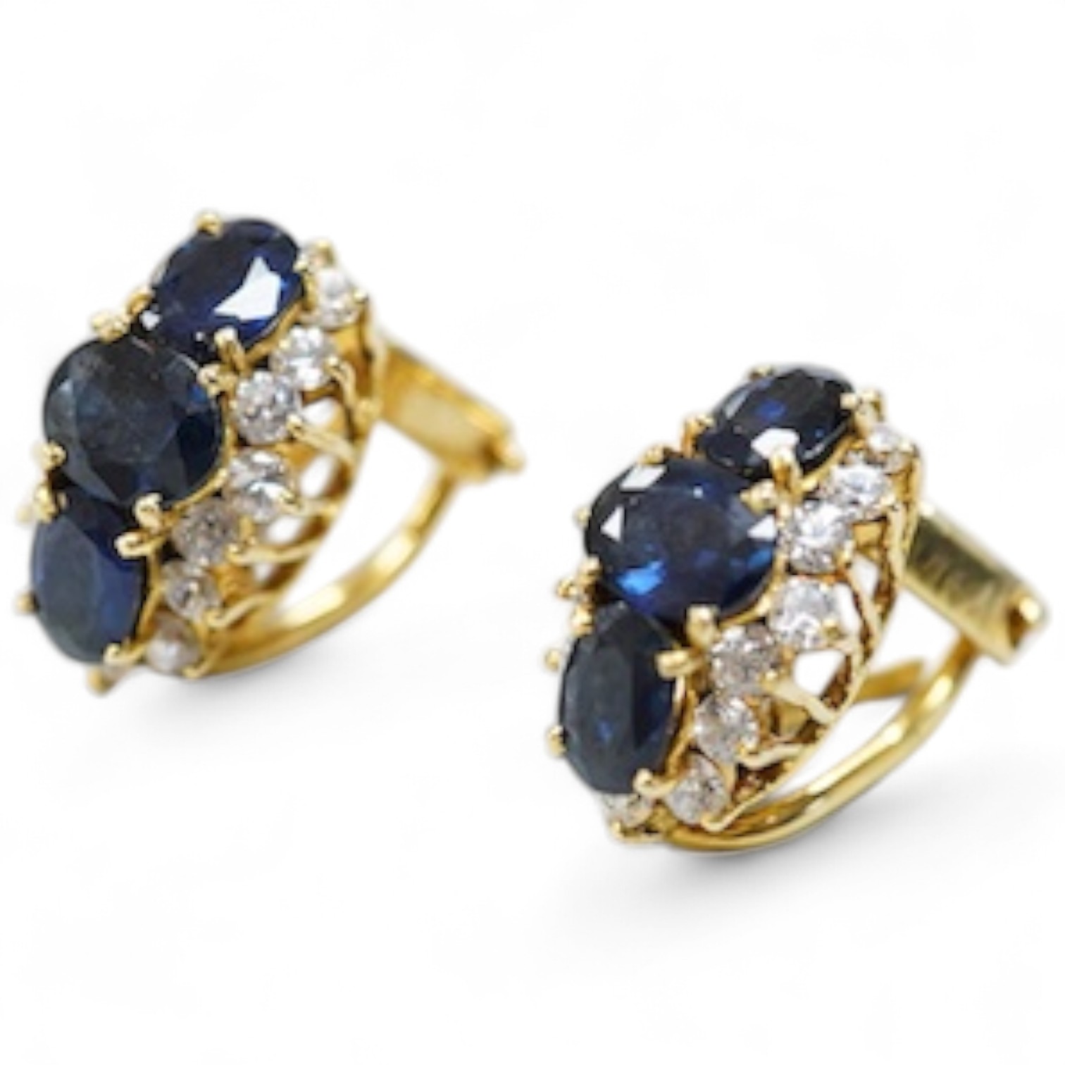 A pair of sapphire earrings, each set with three oval sapphires, within a border of brilliant-cut cubic zirconias, mounted in gold, length 1.4cm each, clip and retractable post fittings